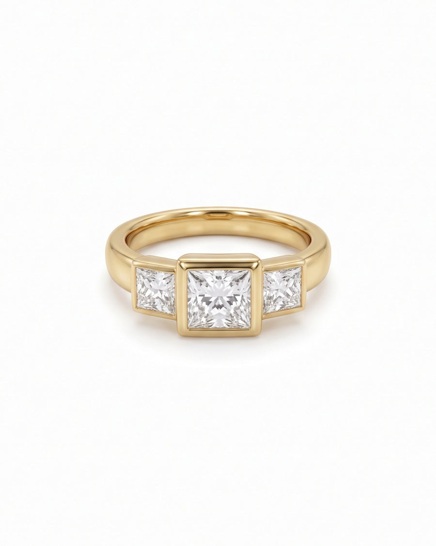 Gold trilogy engagement ring featuring three princess cut diamonds in a bezel setting.
