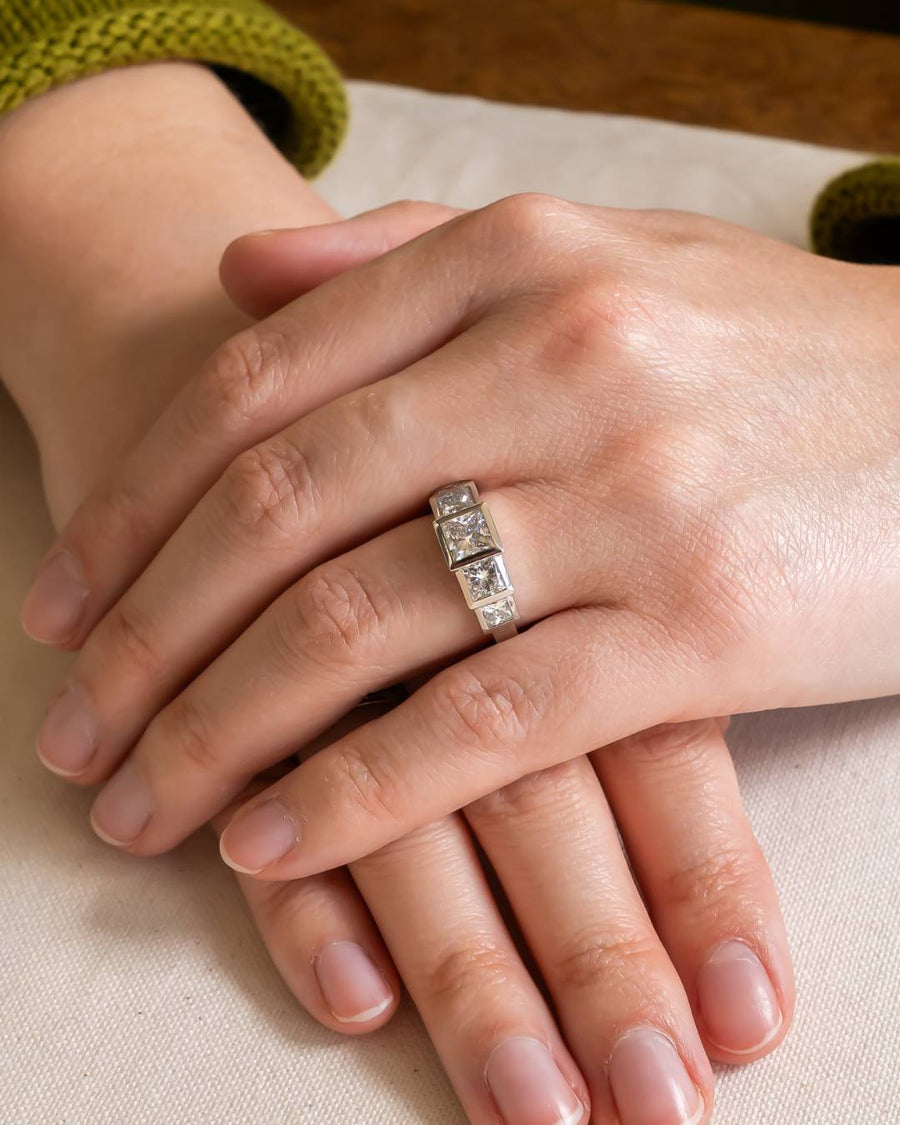 Silver ring with three princess-cut diamonds on a hand.
