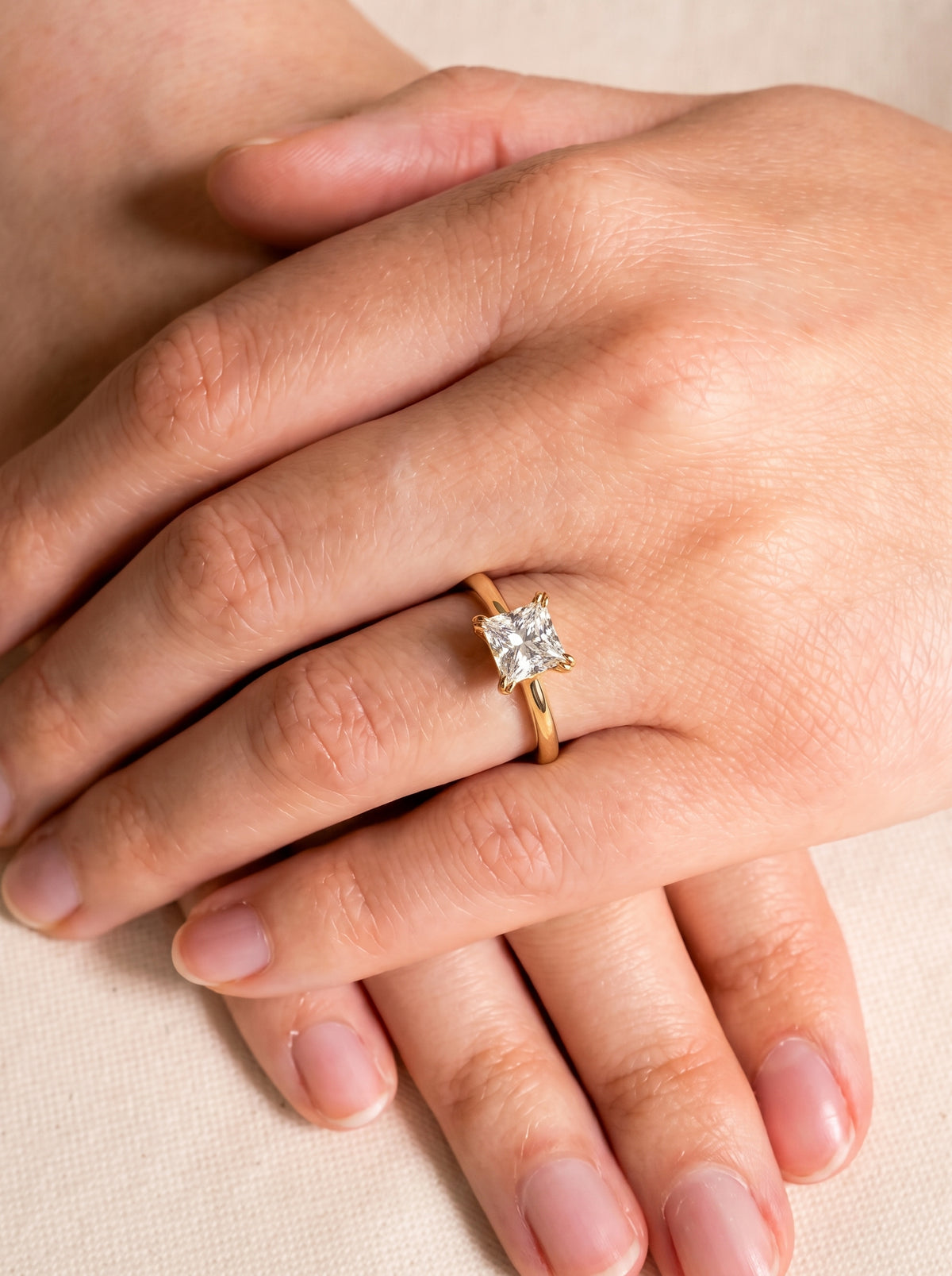 Princess cut diamond engagement ring with a hidden halo on a yellow gold band worn on a finger.