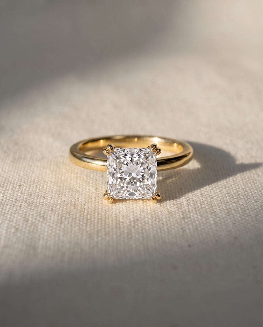 Princess cut diamond engagement ring with a hidden halo on a polished yellow gold band.