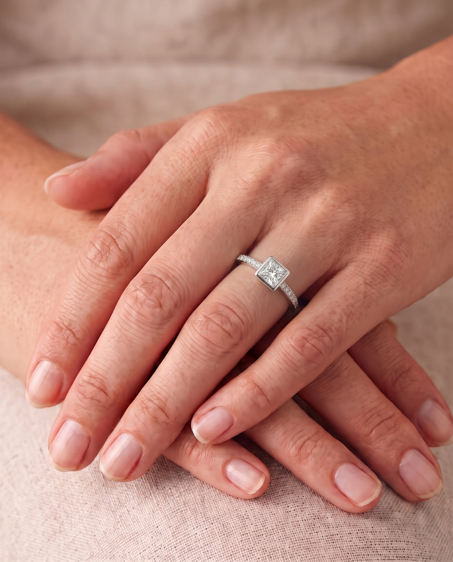 Princess cut diamond engagement ring with a pavé band and bezel setting on a silver metal band.
