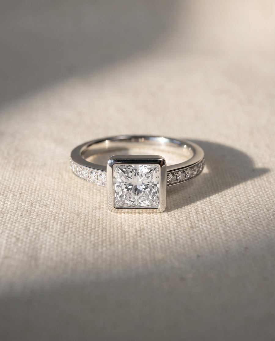 Platinum princess cut engagement ring with a bezel-set center diamond and pavé diamond band.