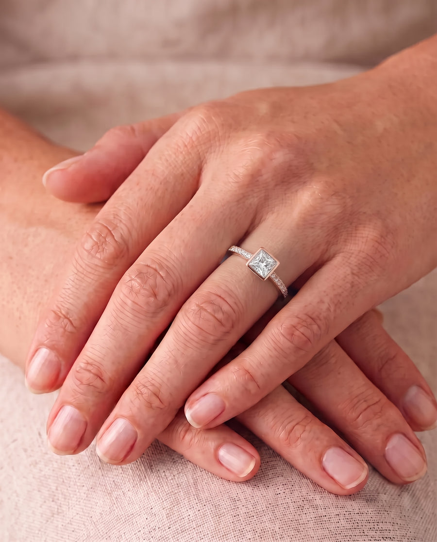 Rose gold engagement ring with a princess cut diamond in a bezel setting and a pavé band.