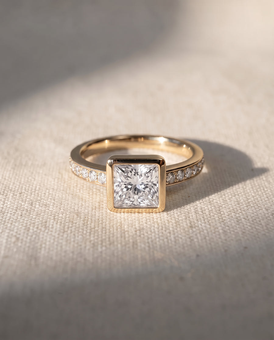 Princess cut diamond engagement ring in 18ct yellow gold with a bezel setting and pavé diamond band.