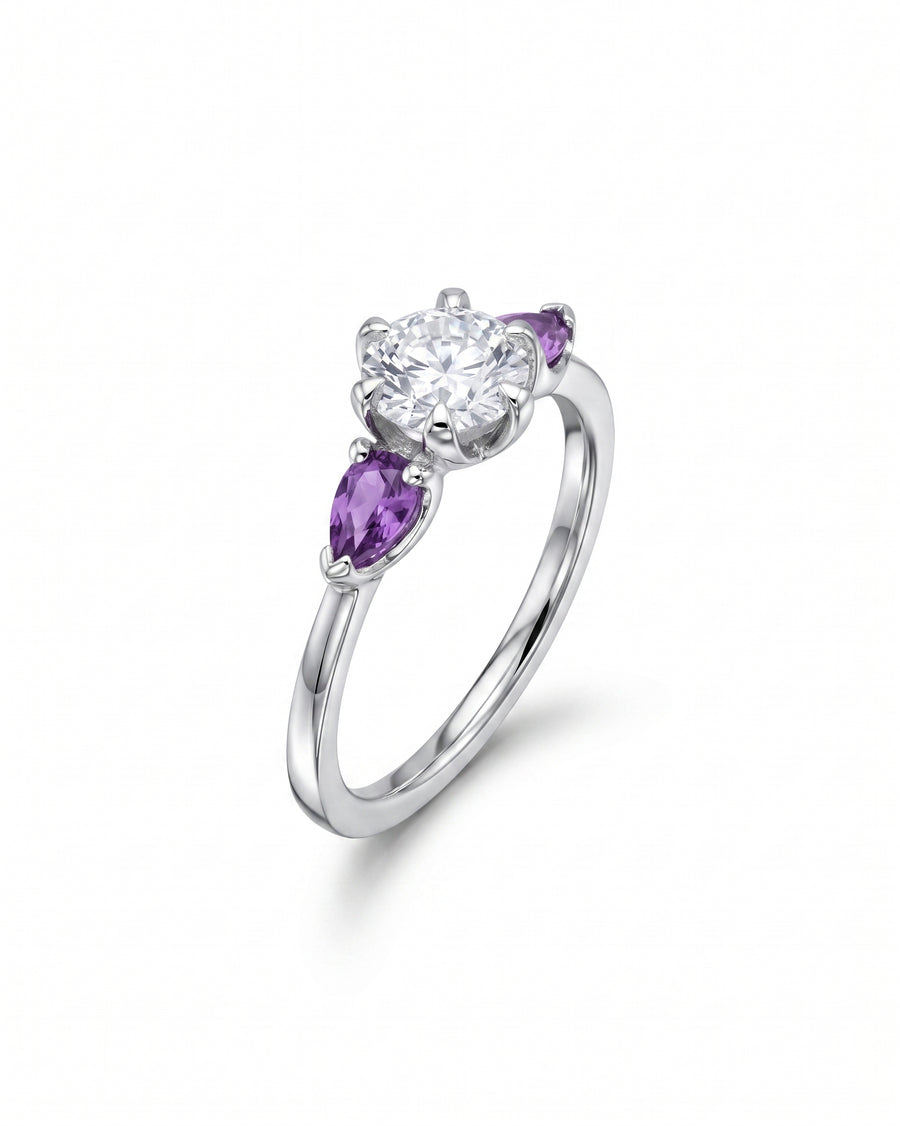 Silver ring with a round diamond flanked by two pear-shaped purple sapphires.
