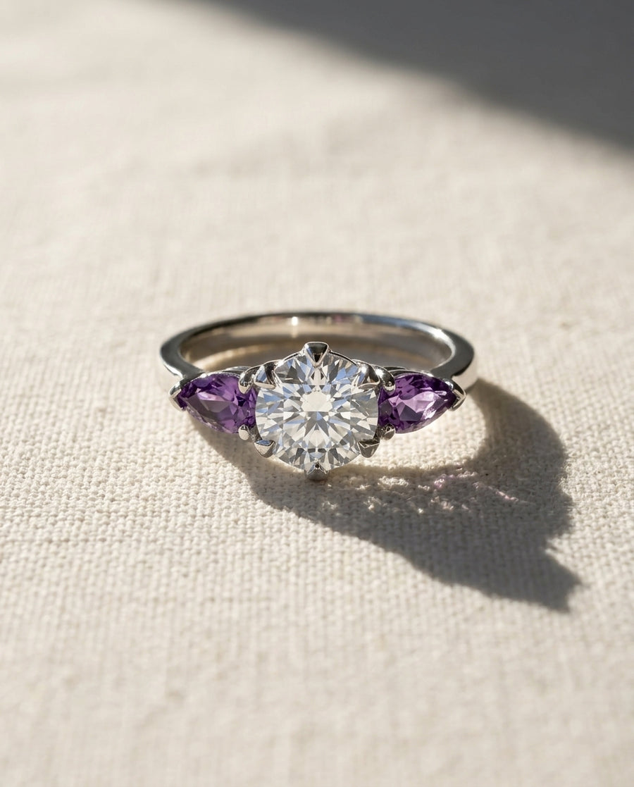 Silver ring with a round diamond flanked by two purple sapphire marquise gemstones.