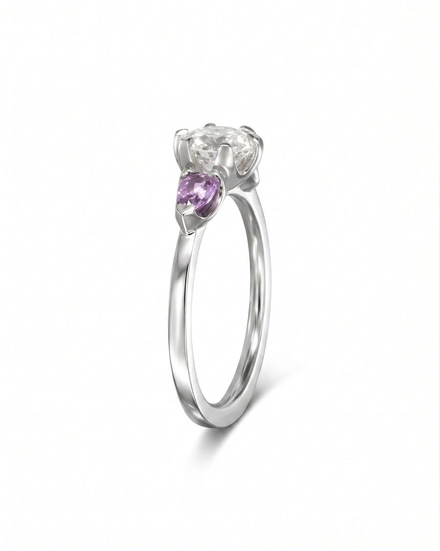 Silver ring with a large clear diamond and two smaller purple sapphire side stones.