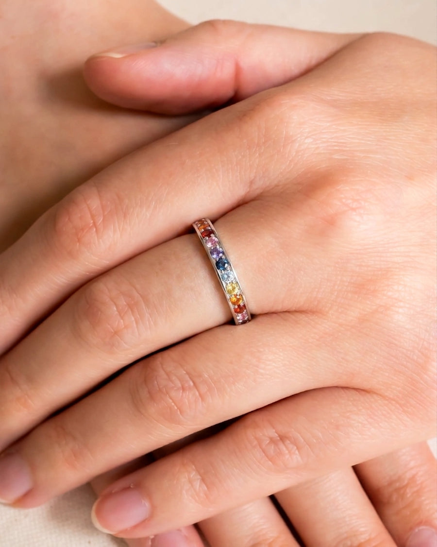Silver eternity ring with rainbow sapphires on a hand.