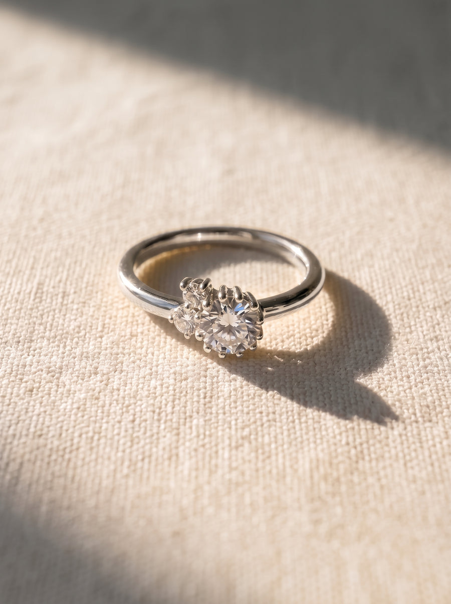 Silver engagement ring with a cluster of round diamonds in a claw setting on a textured fabric surface.