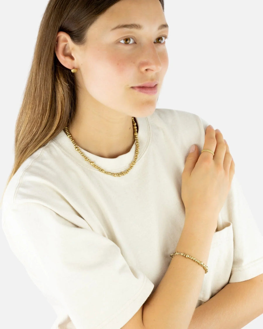 Woman wearing a chunky yellow gold nugget necklace, bracelet, and ring, minimalist style