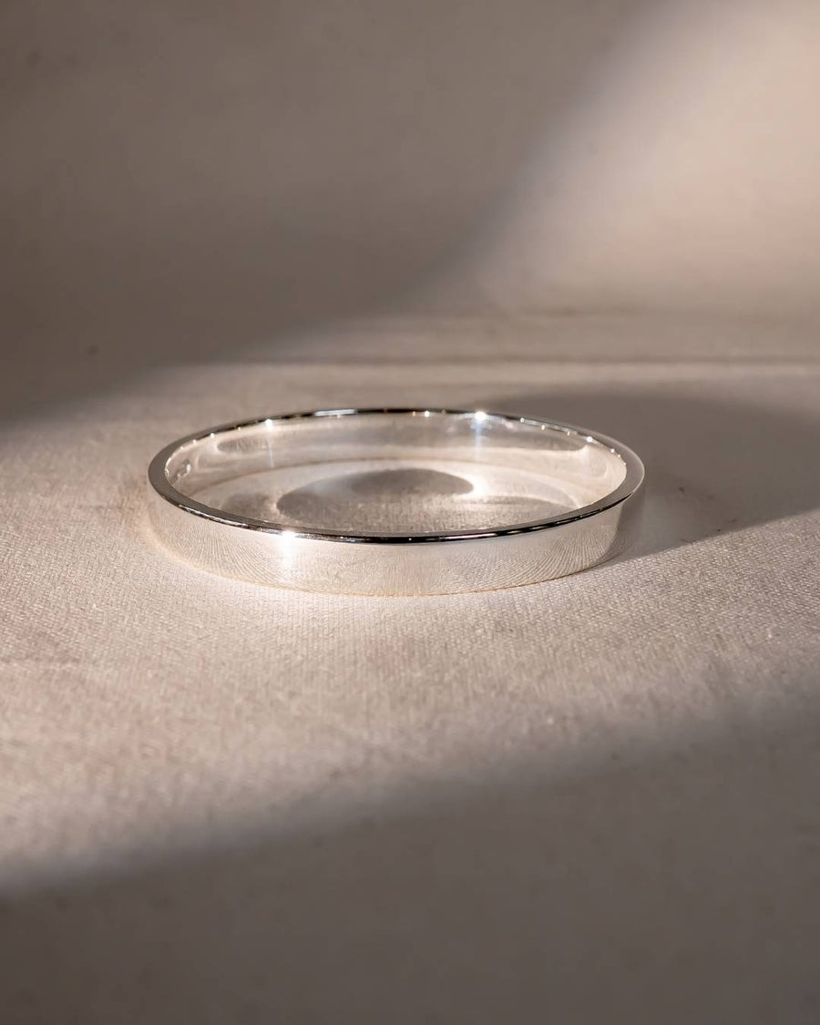 Handcrafted silver bangle bracelet with a smooth finish on a neutral fabric background