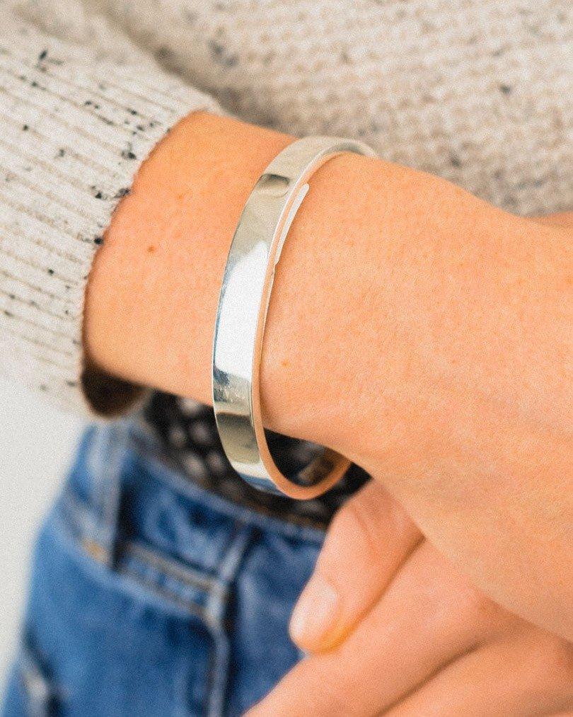 Hand wearing a chunky solid silver rectangular bangle with a polished finish