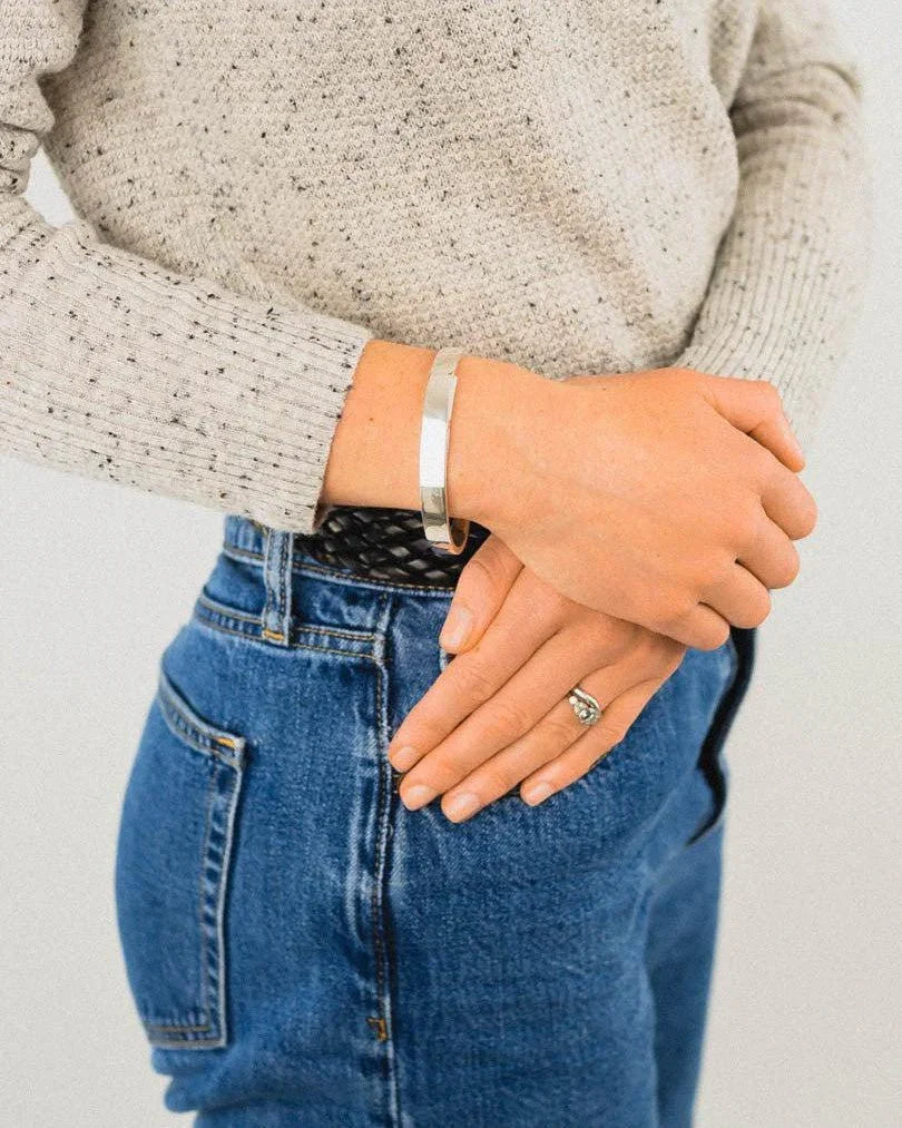Rectangular solid silver bangle worn on wrist, paired with jeans and a knit sweater