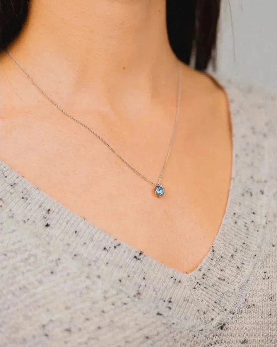 White gold necklace with aquamarine pendant worn on a woman's neck
