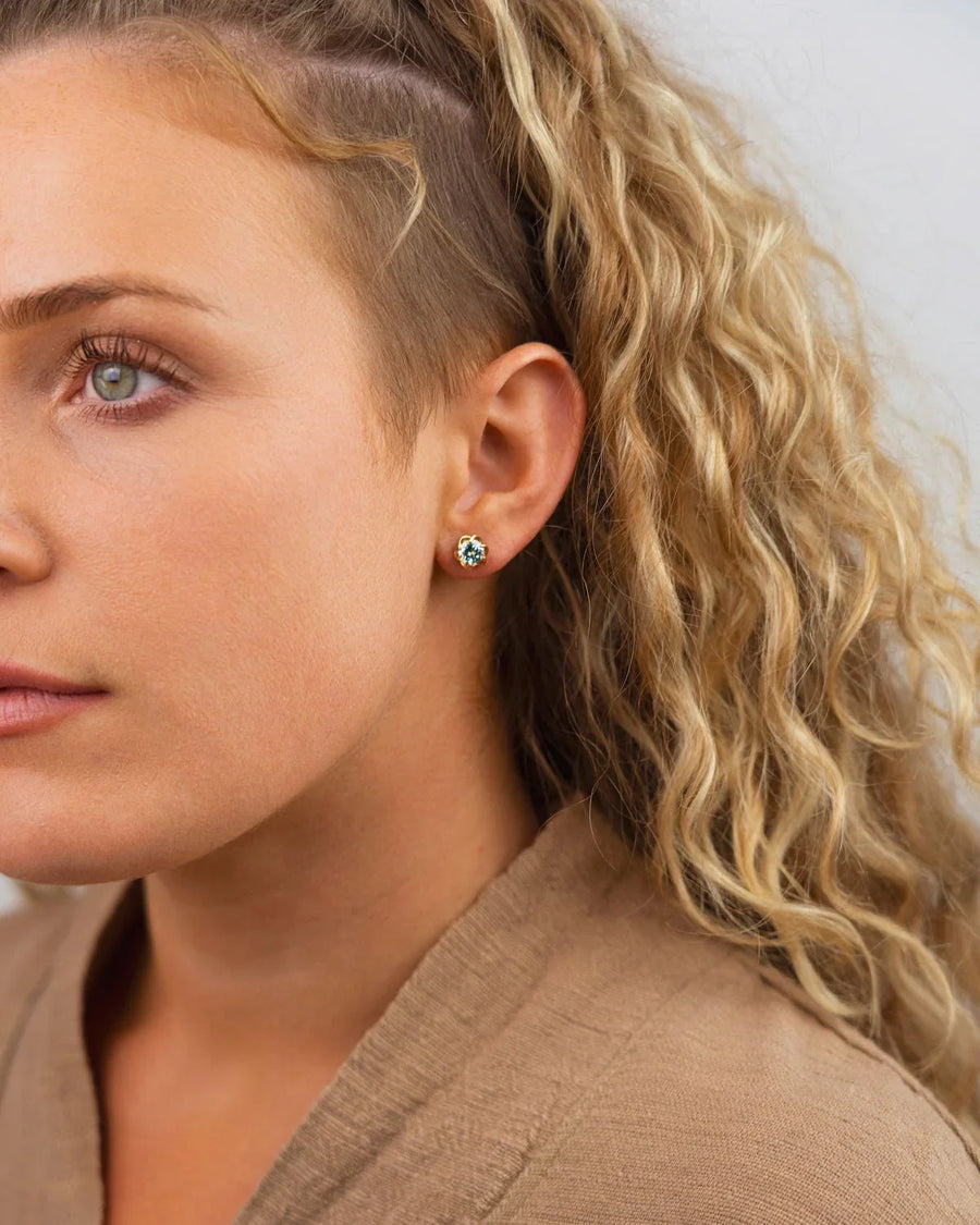 Gold revolved claw gemstone diamond stud earring on an ear.