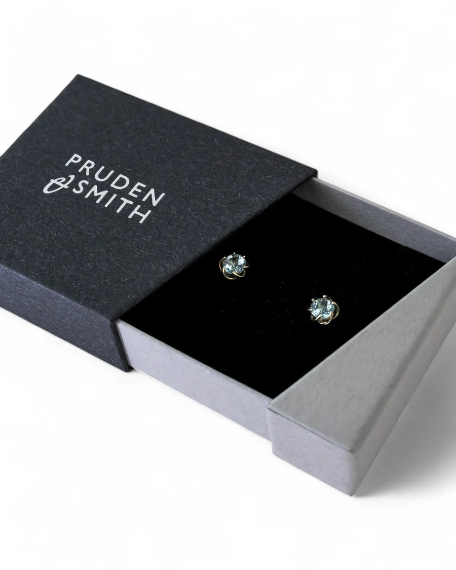 Gold revolved claw gemstone diamond stud earrings in a black box.