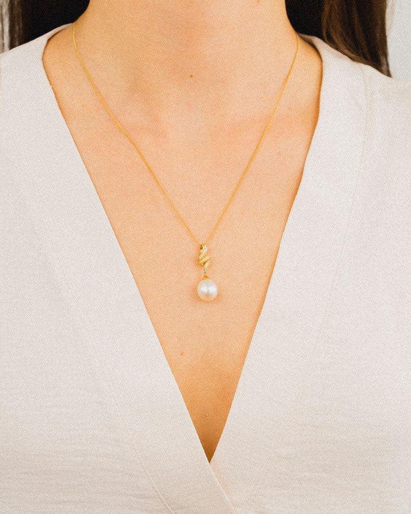 Gold ribbon pendant necklace with pearl and small diamond, worn with a v-neck blouse