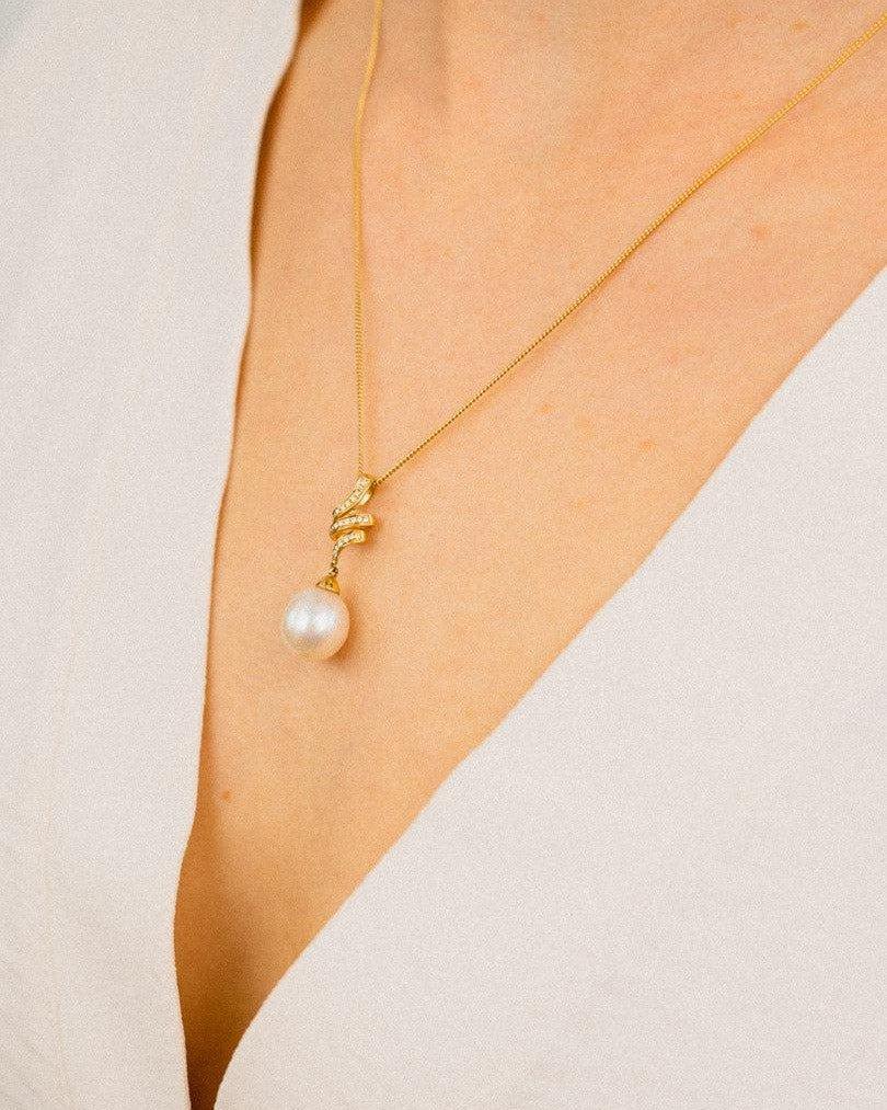 Gold necklace with pearl and diamond pendant on woman in white dress