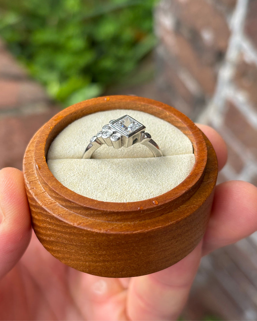 Emerald cut lab-grown diamond engagement ring in a silver band with side bubble accents in a wooden box.