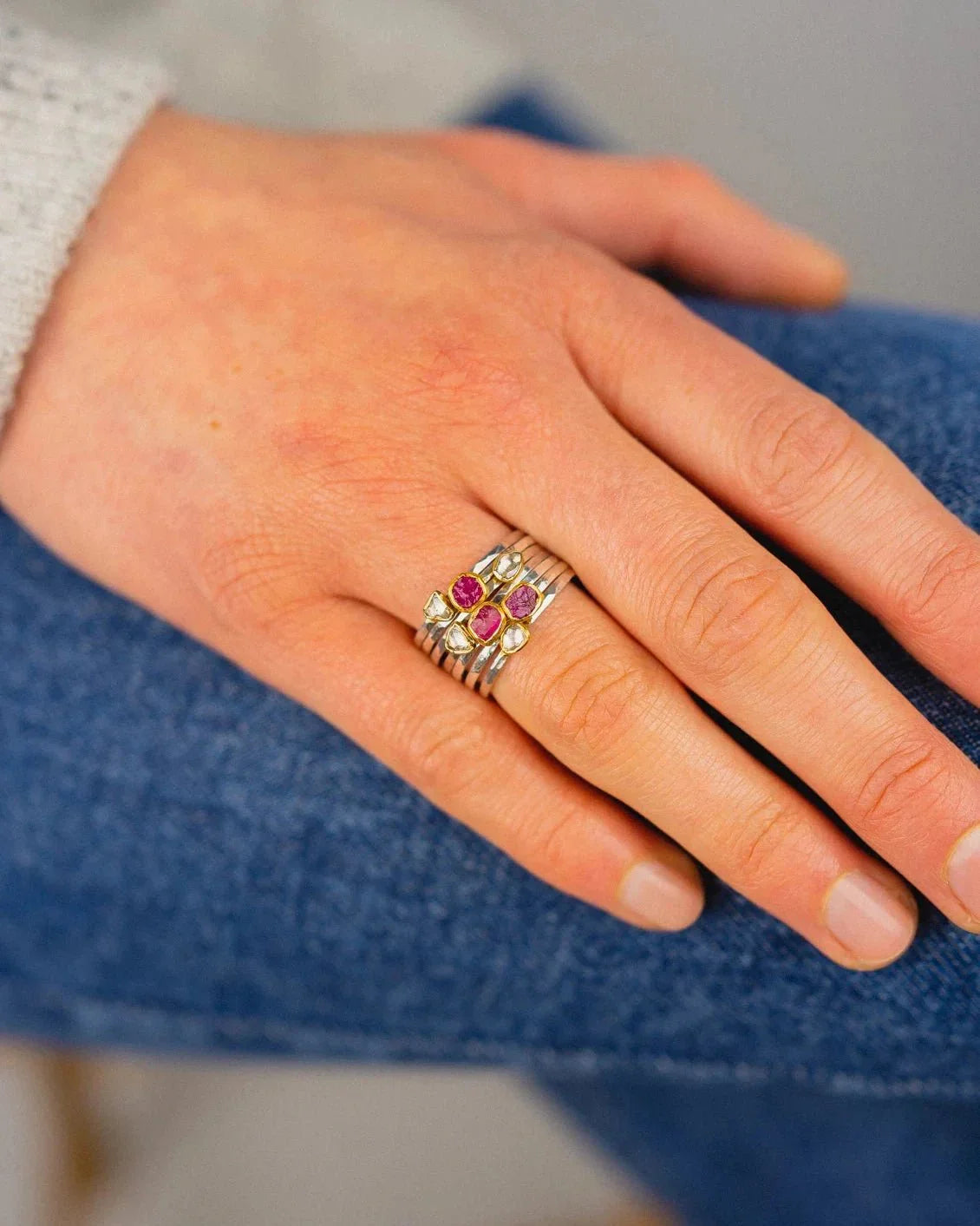 Hand wearing stacked silver rings set with rough-cut rubies and yellow gemstones