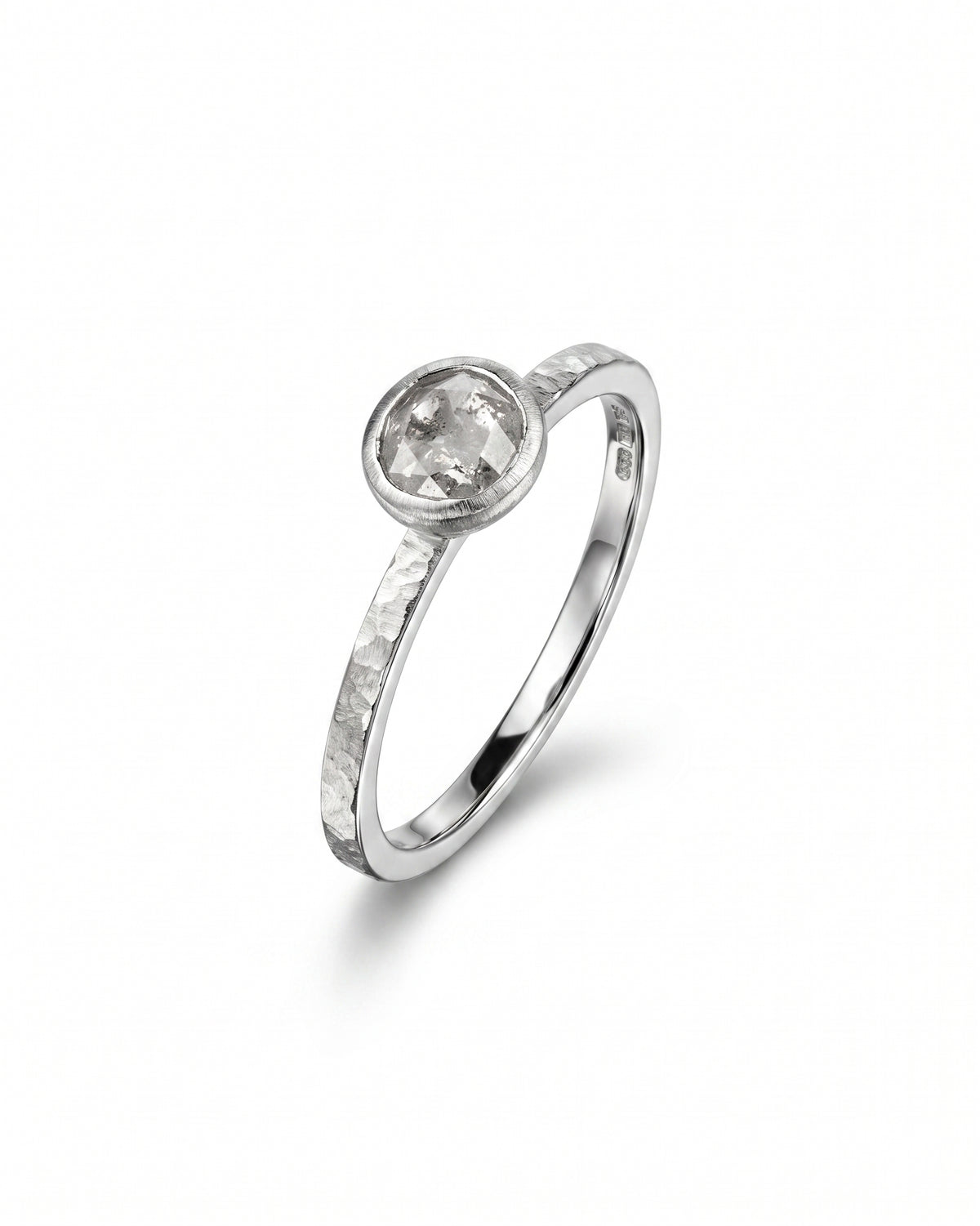 Rough diamond engagement ring in a silver hammered band with a bezel-set round stone.