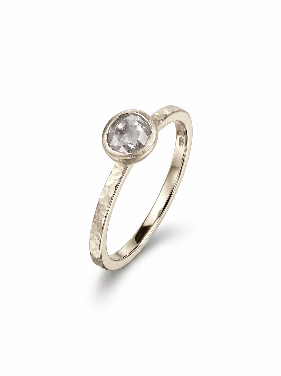 Rough diamond engagement ring with a bezel-set stone on a textured, hammered yellow gold band.