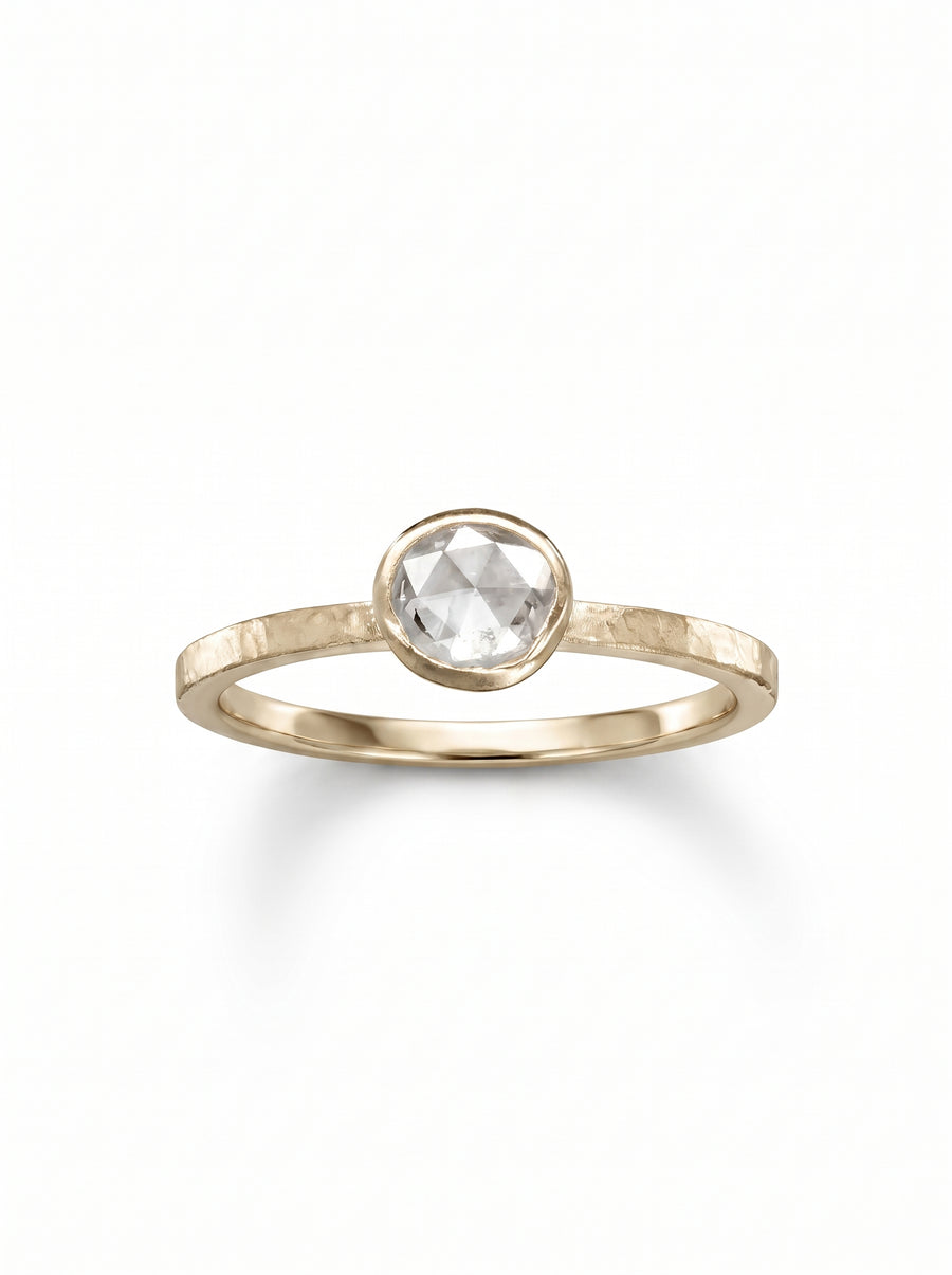 Gold engagement ring with a round rose-cut diamond in a bezel setting on a hammered band.
