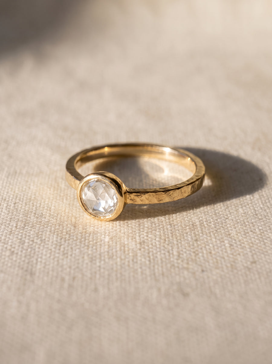 Bezel-set rough diamond engagement ring in 9ct yellow gold with a hammered band texture.