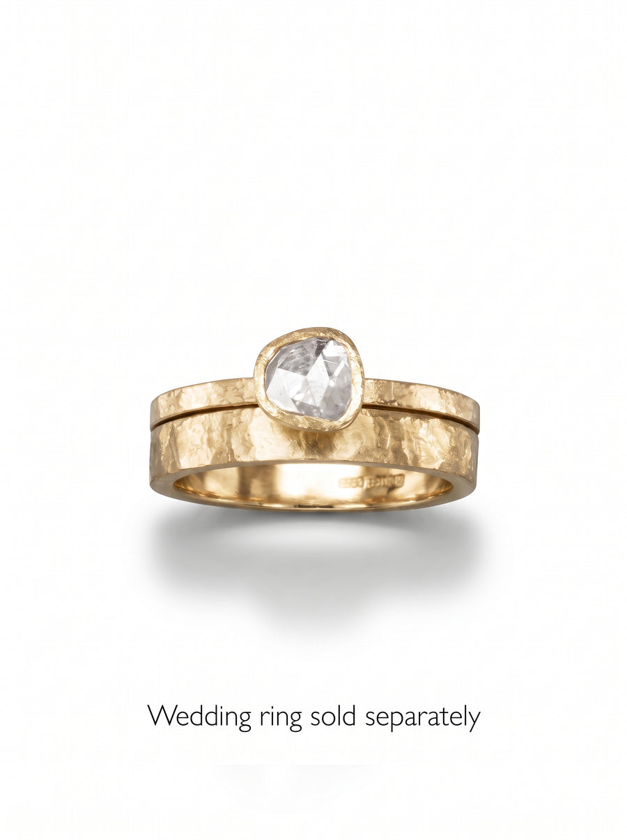 Rough diamond engagement ring with a hammered gold band and a bezel-set, irregular-shaped clear diamond.