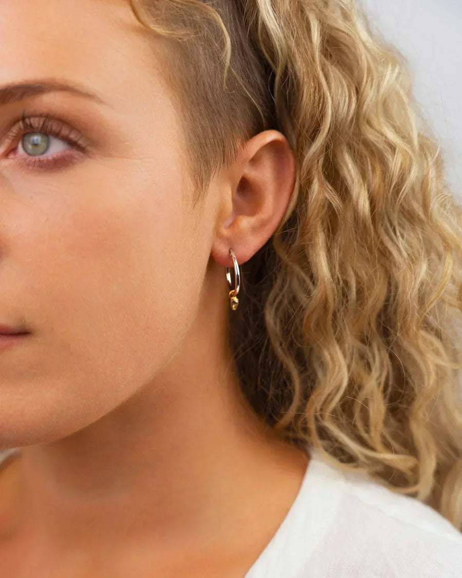 Silver hoop earring with a small gold bead on a woman's ear.