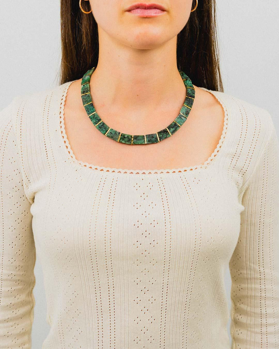 Woman wearing a chunky rough emerald collar necklace with a cream knit top