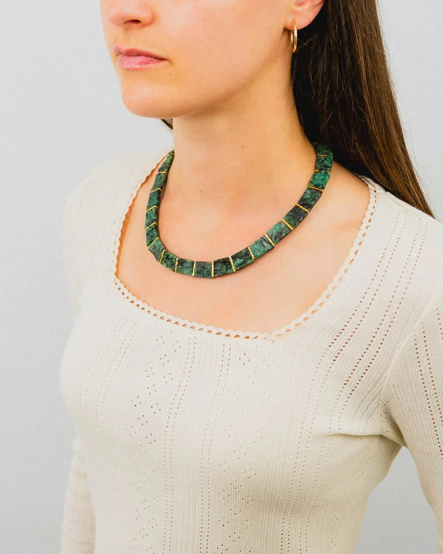 Woman wearing a rough emerald collar necklace with organic, chunky green stones and gold accents