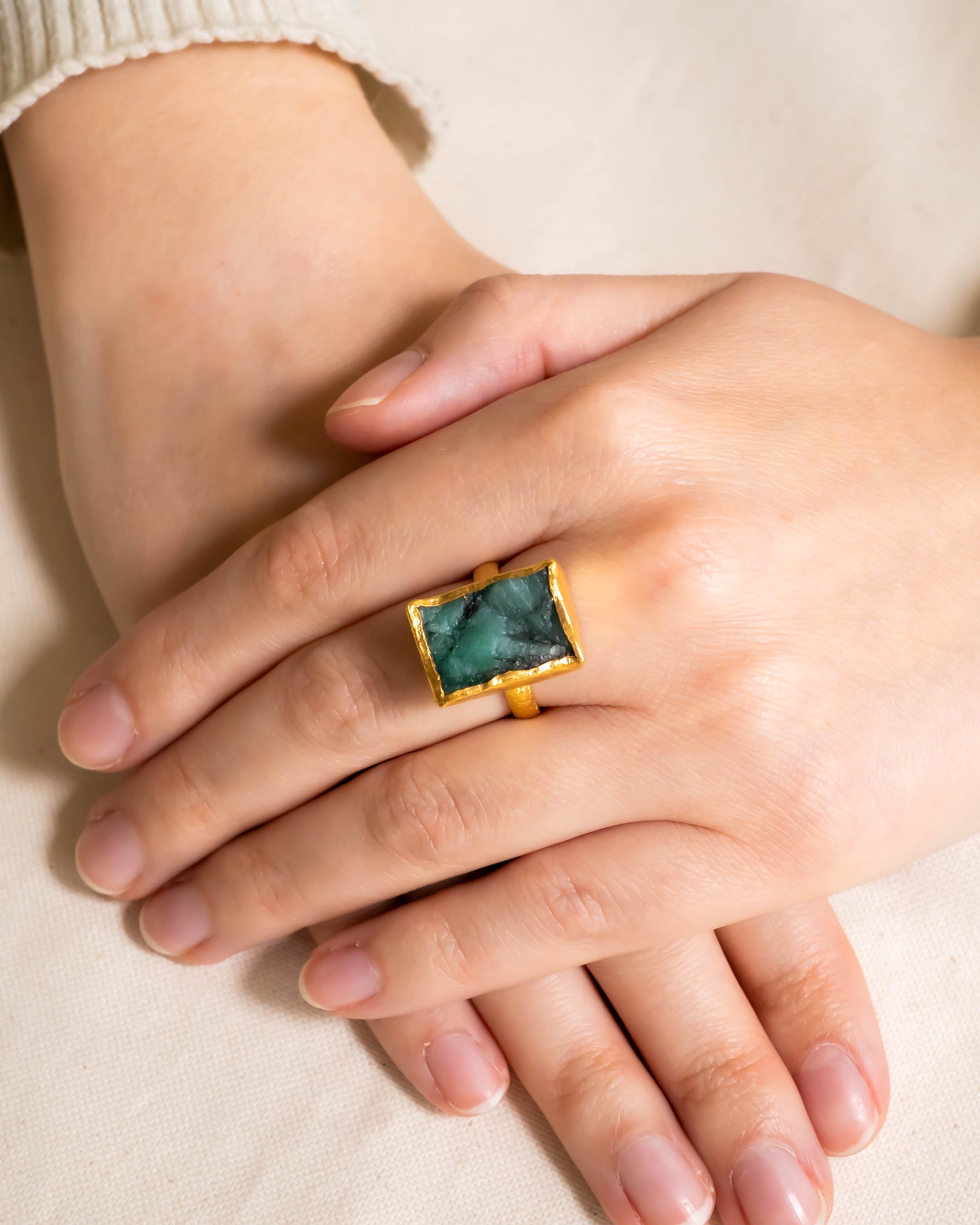 Gold ring with a rectangular rough emerald on a person's hand.