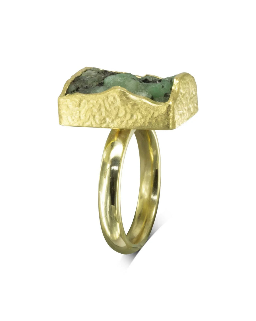 Gold ring with a rough, rectangular emerald gemstone.