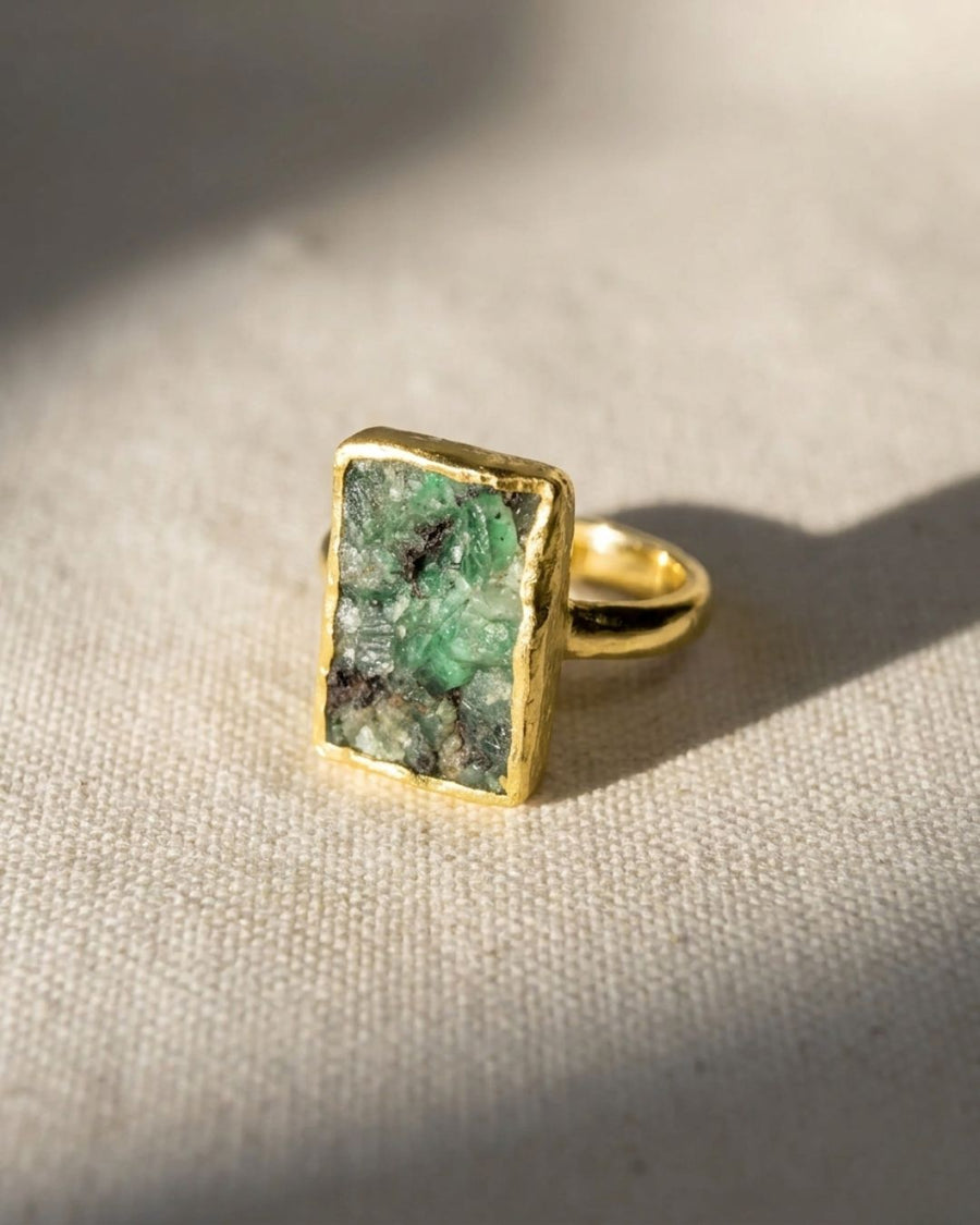 Gold ring with a rectangular rough emerald gemstone.