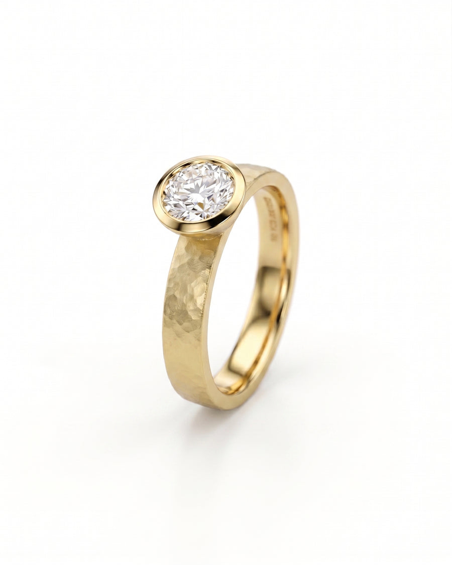 Gold hammered bezel engagement ring with a round brilliant cut diamond.