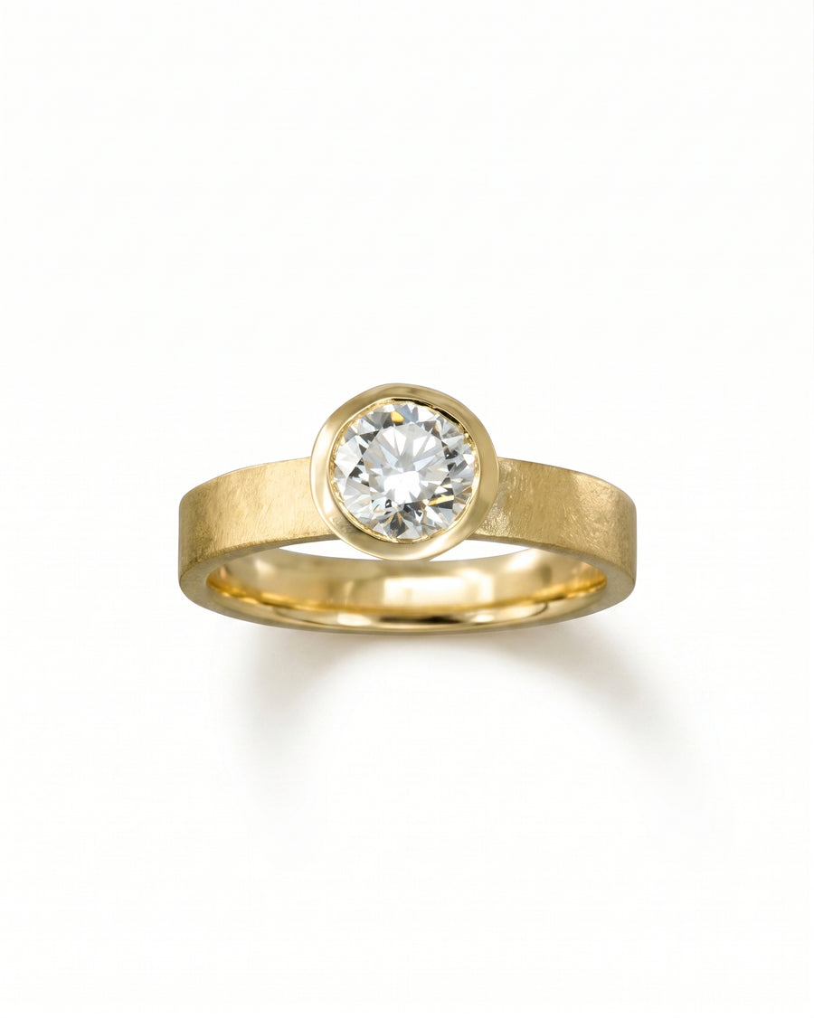 Gold engagement ring with a rough hammered bezel and round brilliant cut diamond.