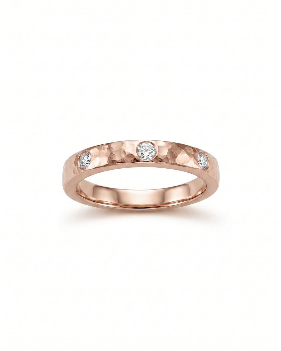 Rose gold rough hammered diamond ring with three round diamonds.