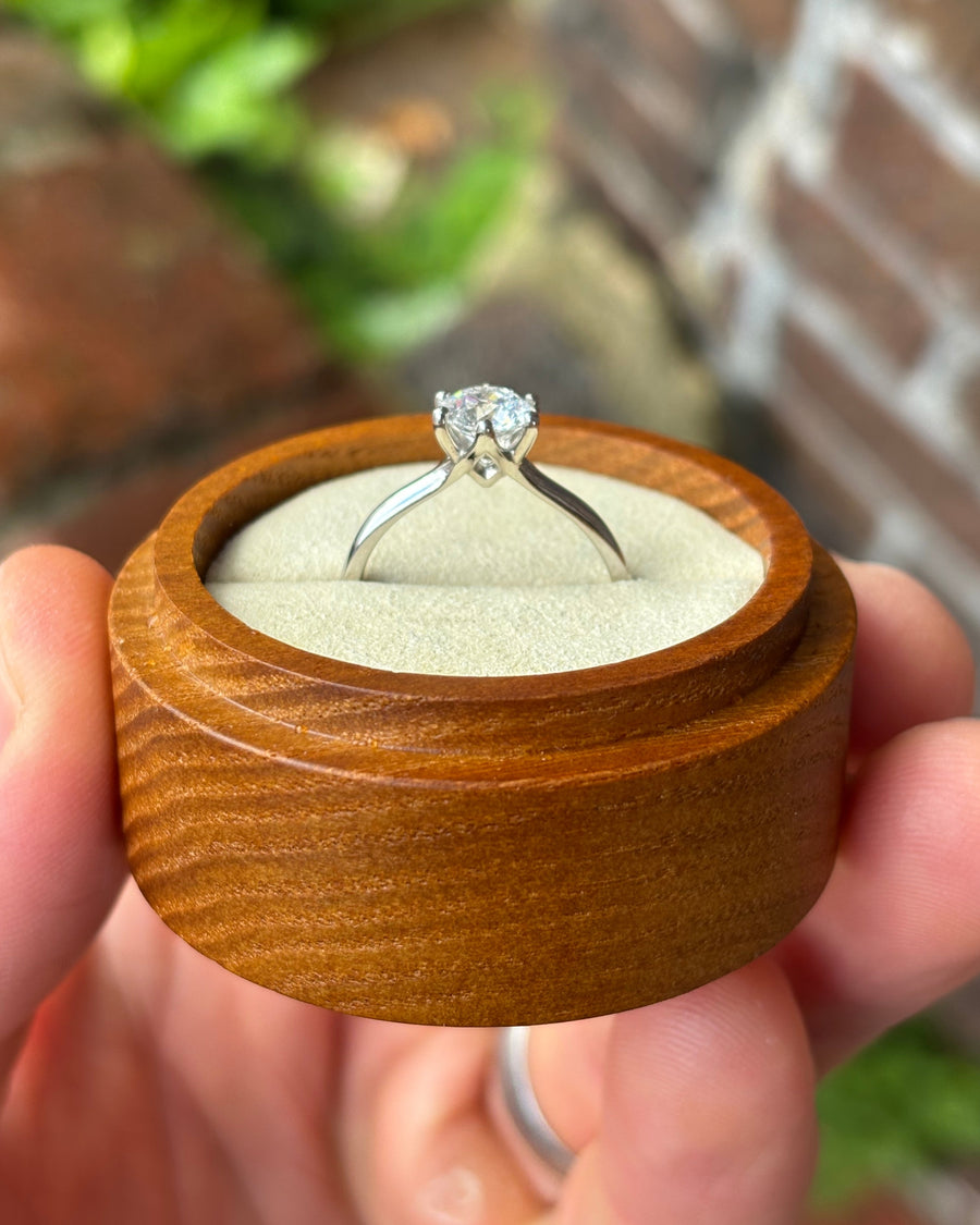 Round cut diamond solitaire engagement ring with a six-claw silver setting in a wooden ring box.