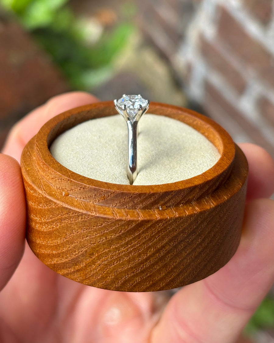 Silver solitaire engagement ring with a round cut diamond in a six-claw setting inside a wooden box.
