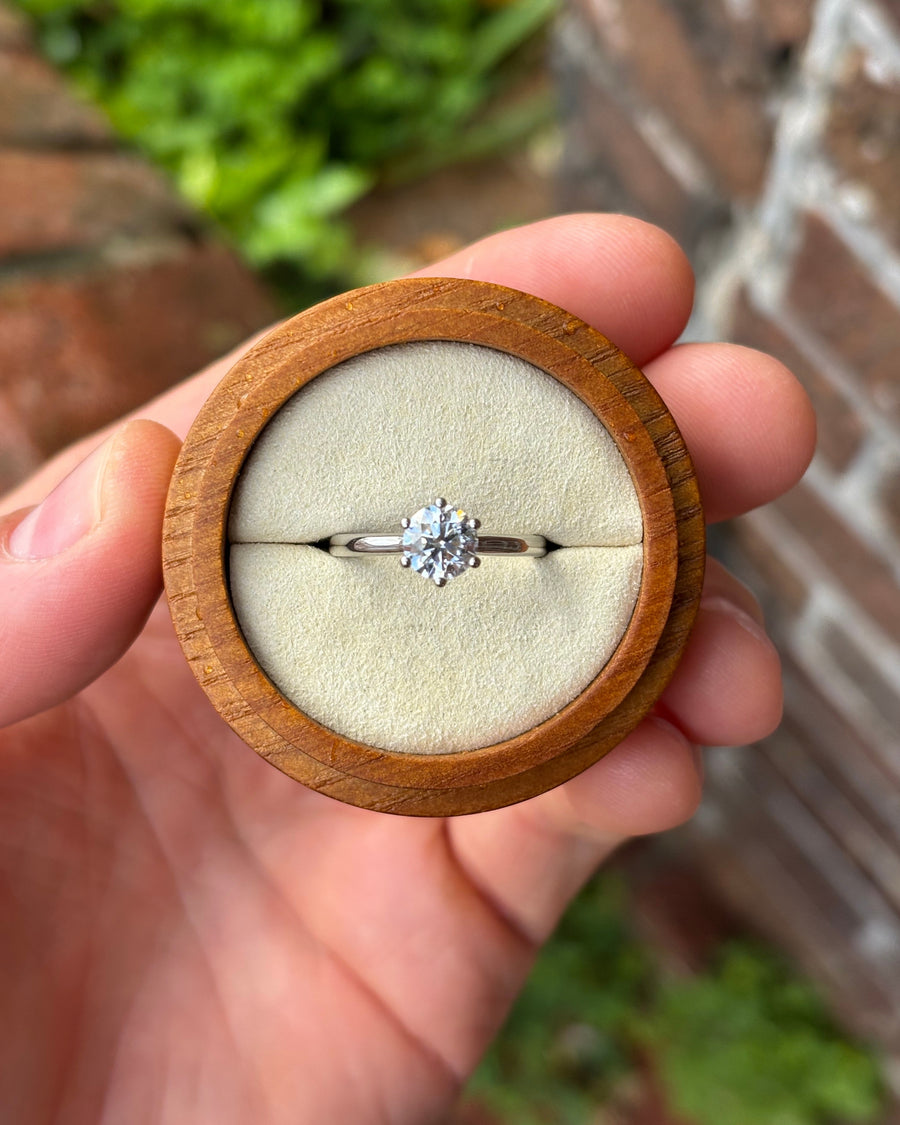 Round cut diamond solitaire engagement ring with a six-claw setting in a platinum band inside a wooden box.