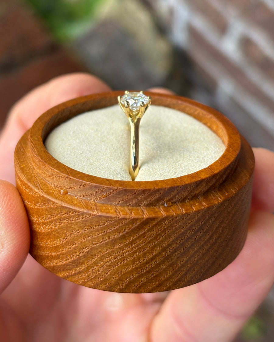 Round cut diamond solitaire engagement ring with a six-claw gold setting in a wooden ring box.