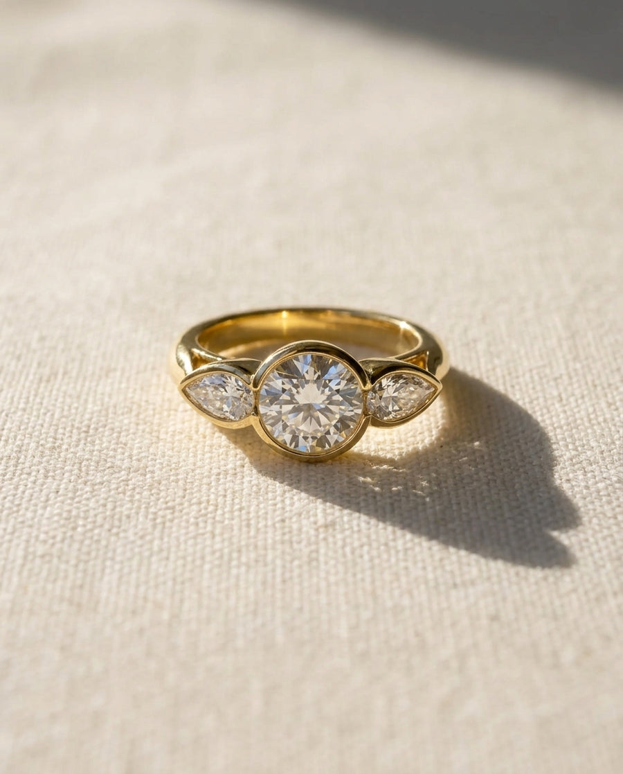 Gold engagement ring with a round brilliant and two pear-shaped diamonds.