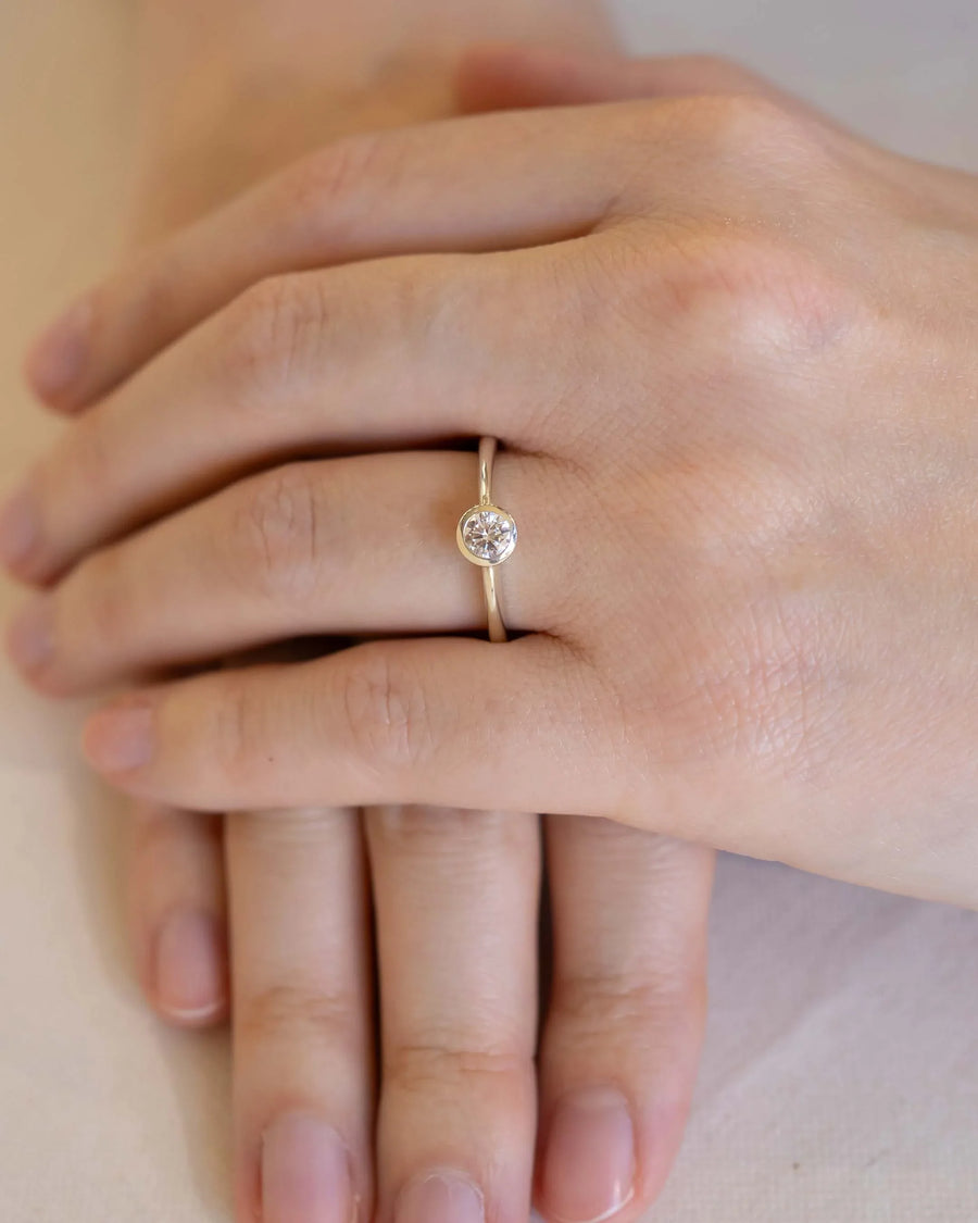 Yellow gold ring with a round cut natural diamond in a bezel setting on a hand.