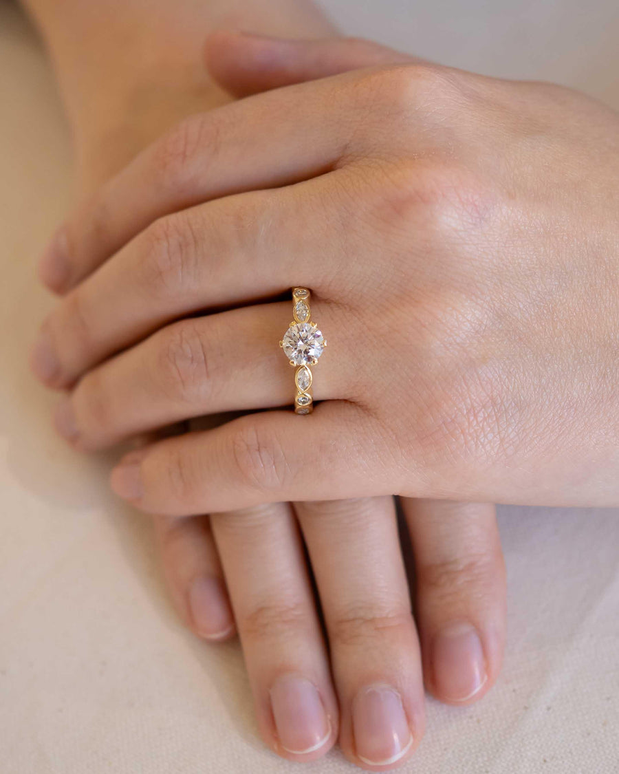 Gold round cut crown set engagement ring with side stones on a hand.