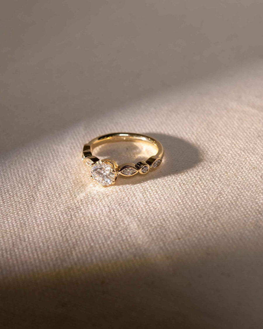 Gold engagement ring with a round cut diamond and marquise-shaped side stones.