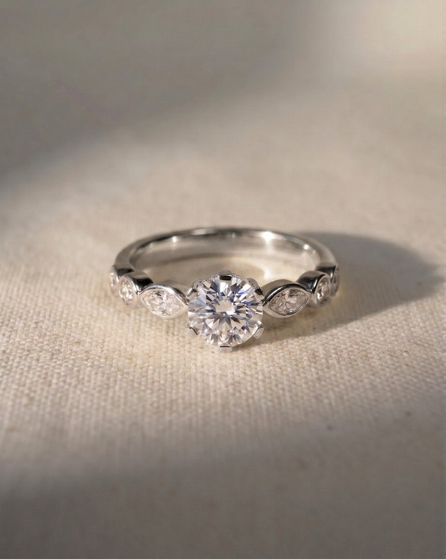 Silver engagement ring with a round cut diamond and marquise side stones.