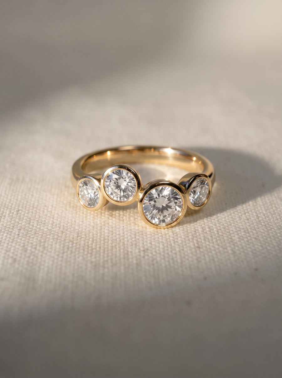 Gold engagement ring featuring four bezel-set round diamonds in a staggered bubble design.