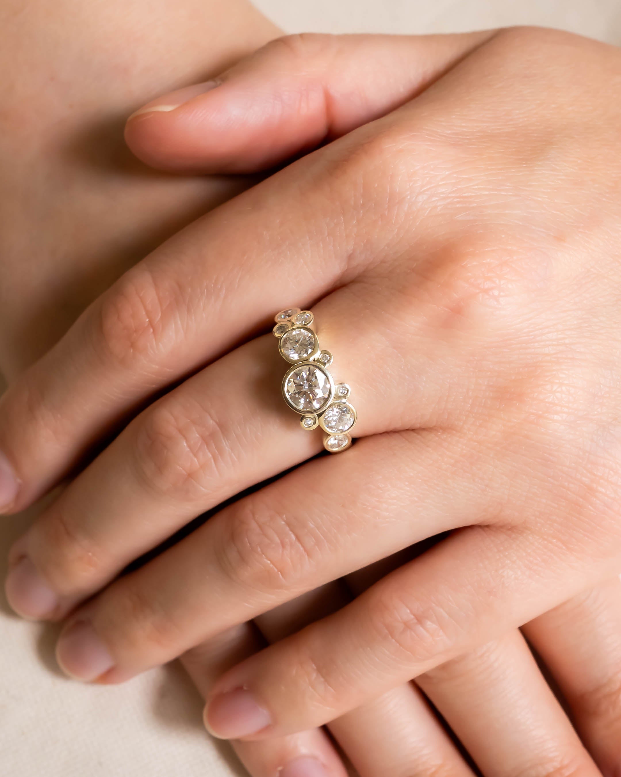 Gold engagement ring with round cut diamonds in a water bubble design on a hand.
