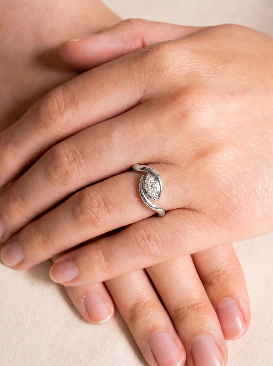 Silver engagement ring with a marquise cut diamond set in a curved, bypass-style band on a finger.